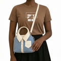 Person wearing a brown t-shirt with a graphic design, holding a blue handbag with a white collar and button details.