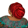 Woman wearing a red satin turban and a teal embroidered outfit on a white background