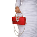 Red handbag with pearl handle held by a person wearing a white dress.