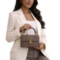 Woman holding a brown handbag with gold accents against a white background
