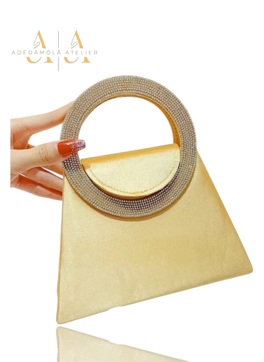 Beige handbag with a round, embellished handle held by a hand with red nail polish on a white background.