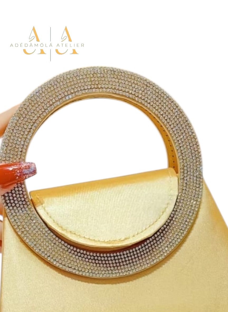 Beige handbag with a round, embellished handle held by a hand with red nail polish on a white background.