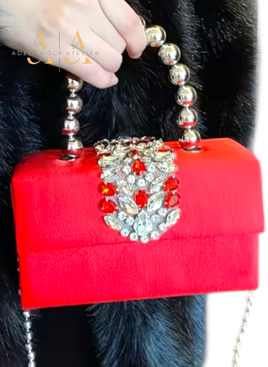 Red clutch bag with decorative  and beads held by a person wearing a fur coat.