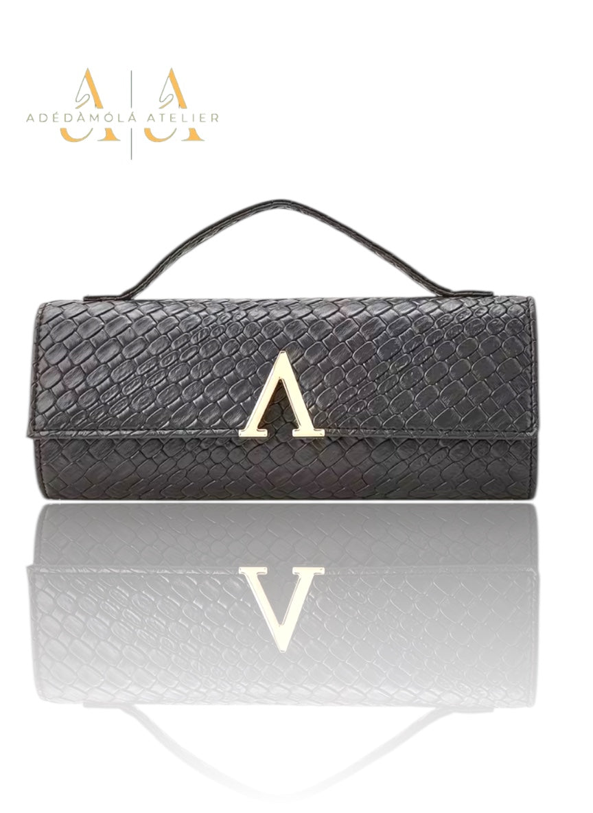 Black textured clutch bag with gold letter 'A' on a reflective surface