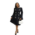 Woman wearing a black dress with white bow patterns, holding a white handbag on a white background