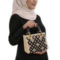 Person holding a decorative handbag with intricate patterns on a white background