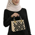Person holding a decorative handbag with intricate patterns on a white background
