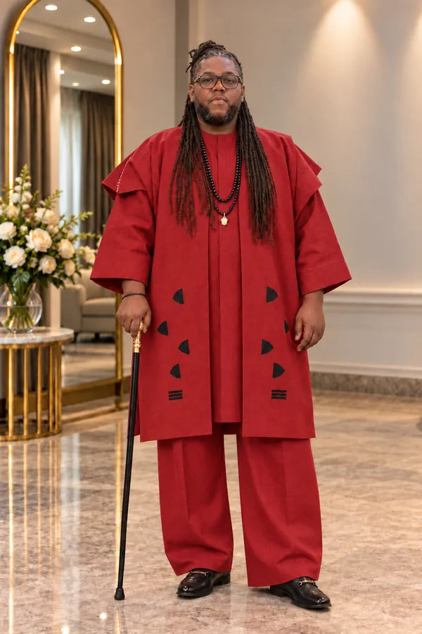 Man wearing a burgundy traditional ensemble with a long tunic, matching trousers, a patterned outer garment and black beads.